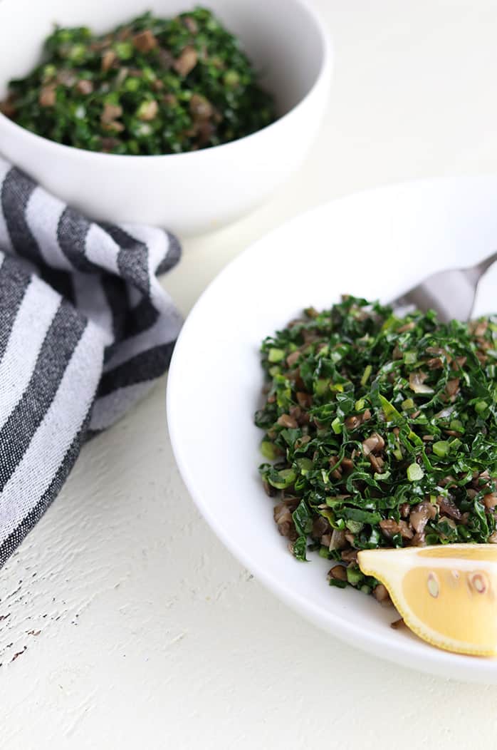 sauteed kale with mushrooms plated next to a slice of lemon