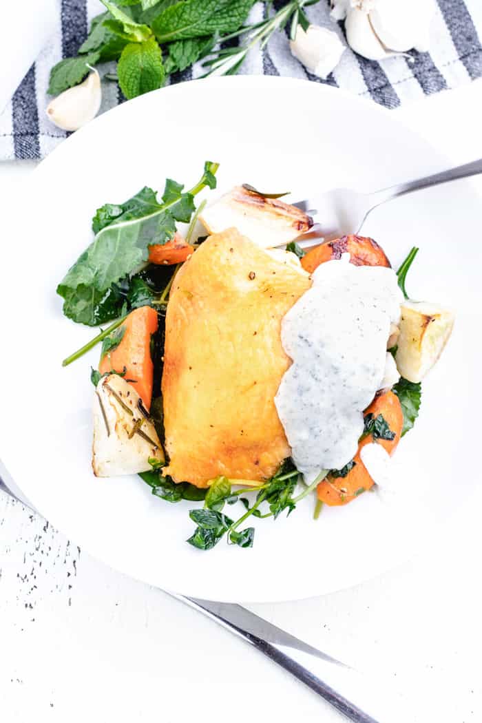 plated chicken on top of roasted vegetables with wilted greens and a mint yogurt sauce